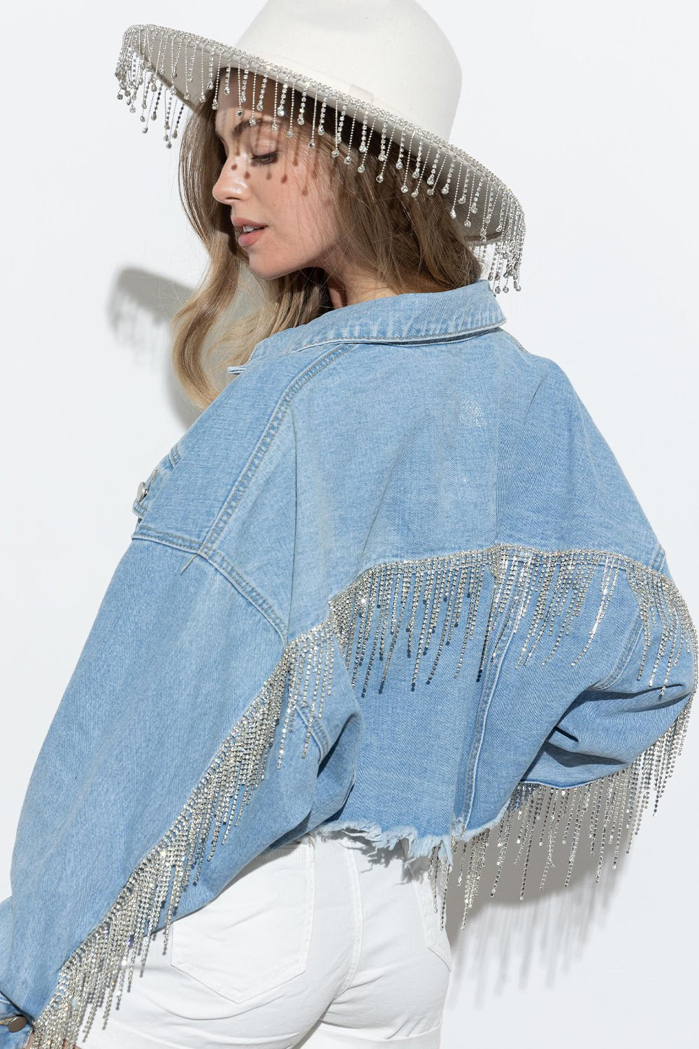 Elevate your denim game with the Crop Frayed Rhinestone Fringe Denim Jacket from Blue B. This boho-chic jacket features a cropped and frayed hem, rhinestone fringe detailing on the sleeves and back, and a stylish Western fashion aesthetic. Perfect for adding a touch of cowgirl style to your wardrobe.